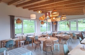 Cozy dining room with wooden furniture and hanging lamps, large windows with a view of the greenery.