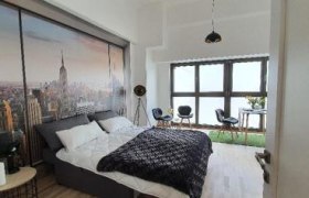 Modernes Schlafzimmer mit großem Bett, Stadtbild-Wandbild und Sitzbereich vor großen Fenstern.