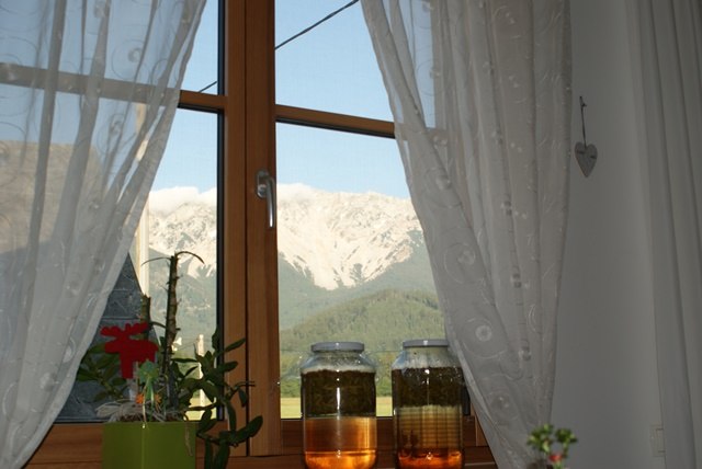 View of a mountain from a window with curtains. Two glasses of liquid are on the windowsill.