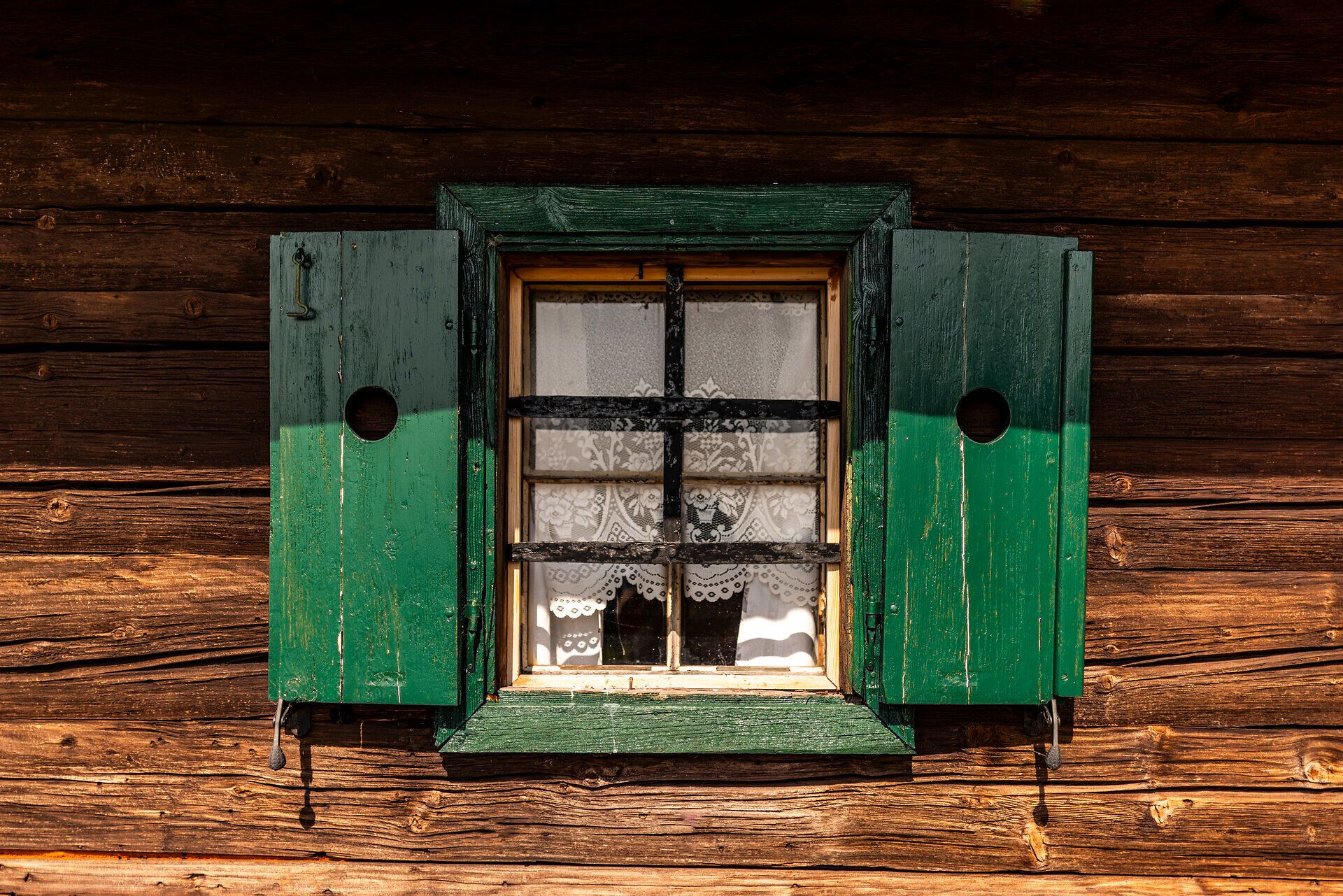 Fenster einer urigen Almhütte mit Fensterläden und Häkelgardine.
