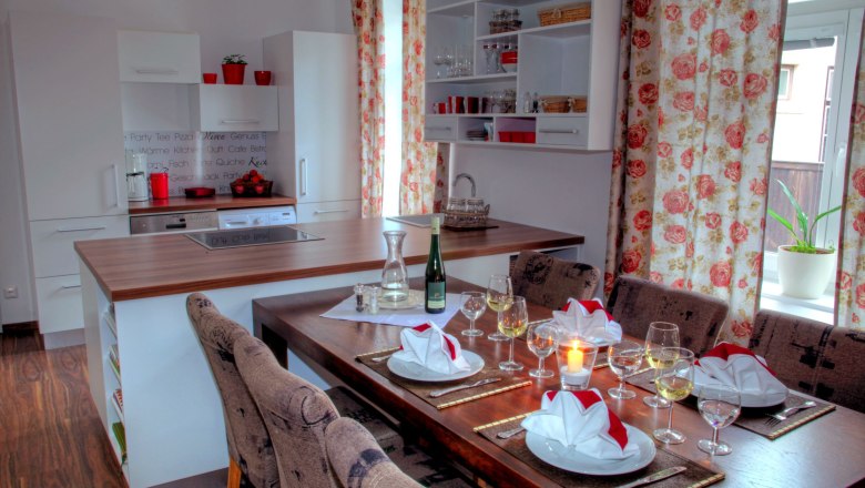 Moderne Küche mit Esstisch, gedeckt mit Gläsern und Servietten, Blumenmuster-Vorhänge.