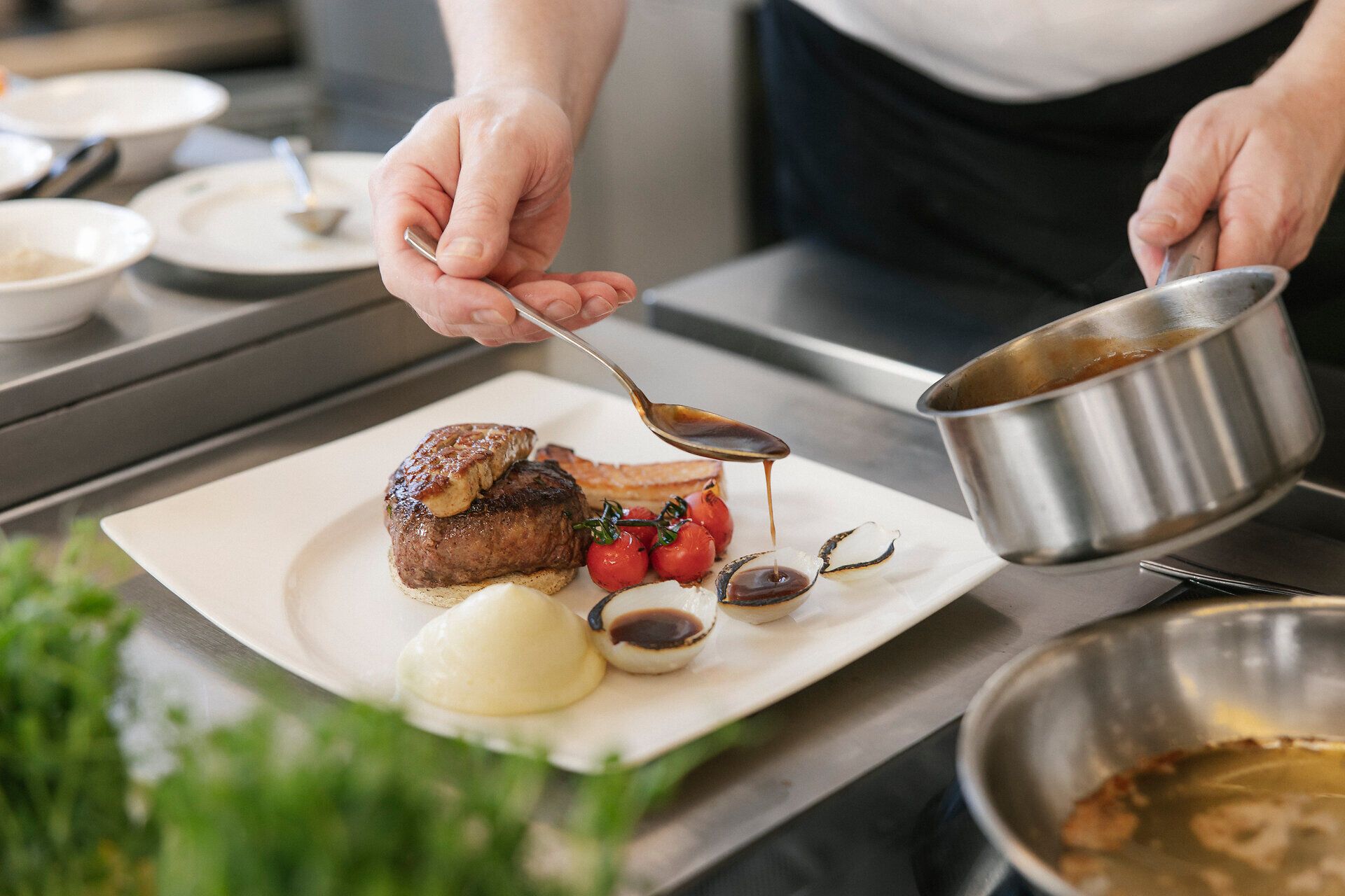 Koch richtet ein Hauptgericht mit Sauce auf einem weißen Teller an.