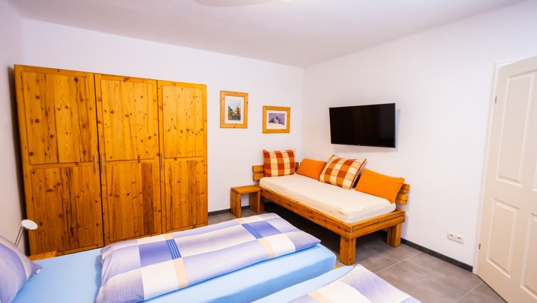 Schlafzimmer mit Holzmöbeln, zwei Betten, Sofa, TV und Bildern an der Wand.