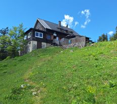 Waldfreundehütte am Obersberg mit Holzverkleidung an einem Hang, davor eine Wiese und blauer Himmel