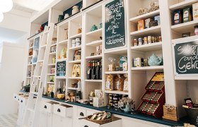 Farm store with white wooden shelves and various products such as spices, chocolates and teas.