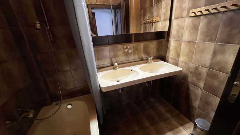 Badezimmer mit braunen Fliesen, Doppelwaschbecken, Badewanne und Spiegel.