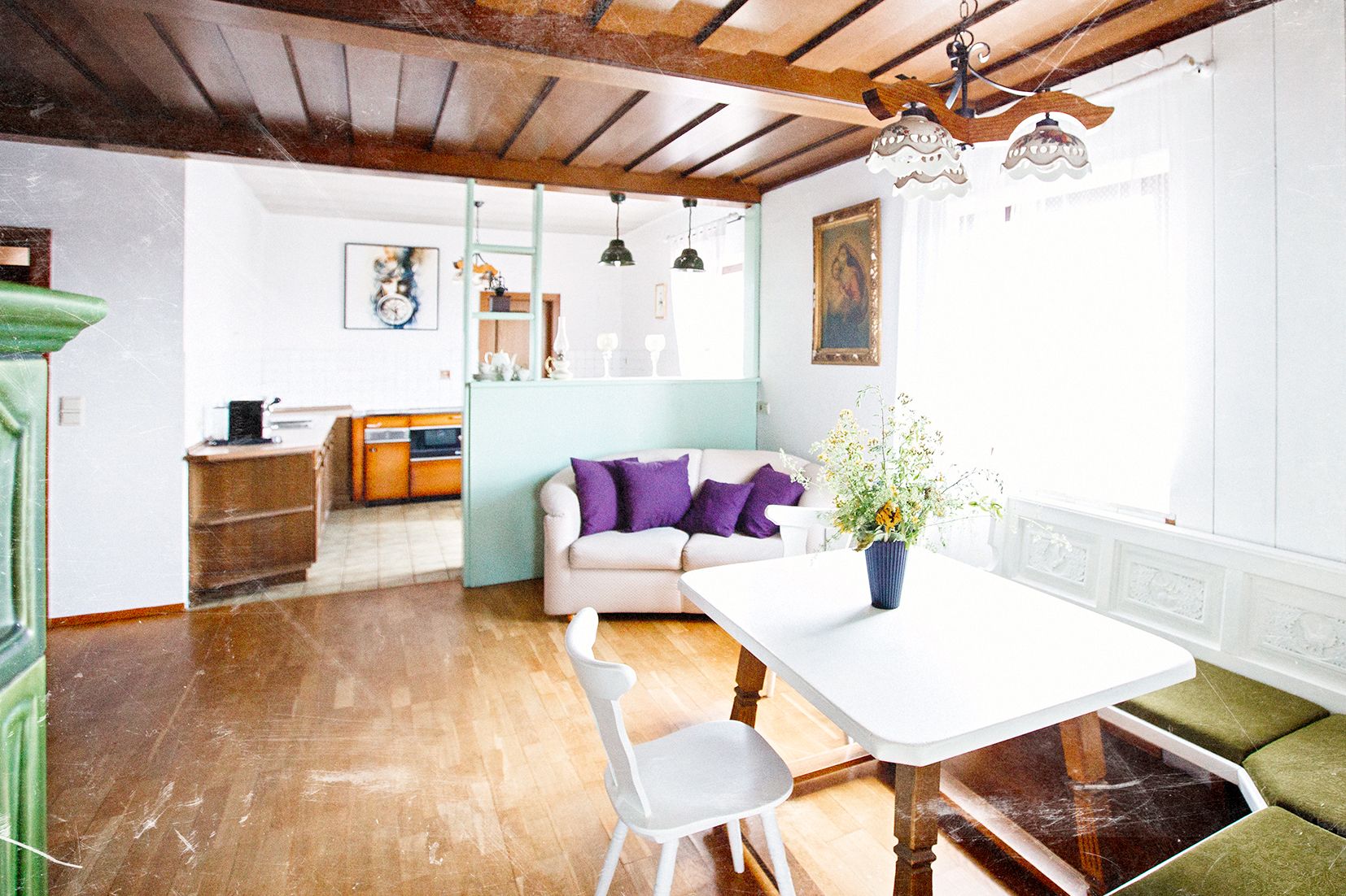 Gemütliches Wohnzimmer mit Holzboden, Sofa, Esstisch und Küche im Hintergrund.