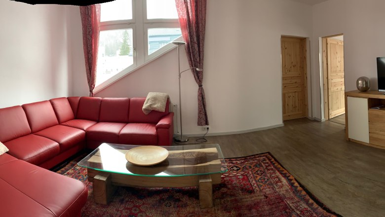 Wohnbereich, © Seidl Wohnzimmer mit rotem Ledersofa, Glastisch, Teppich und TV auf Holzschrank.