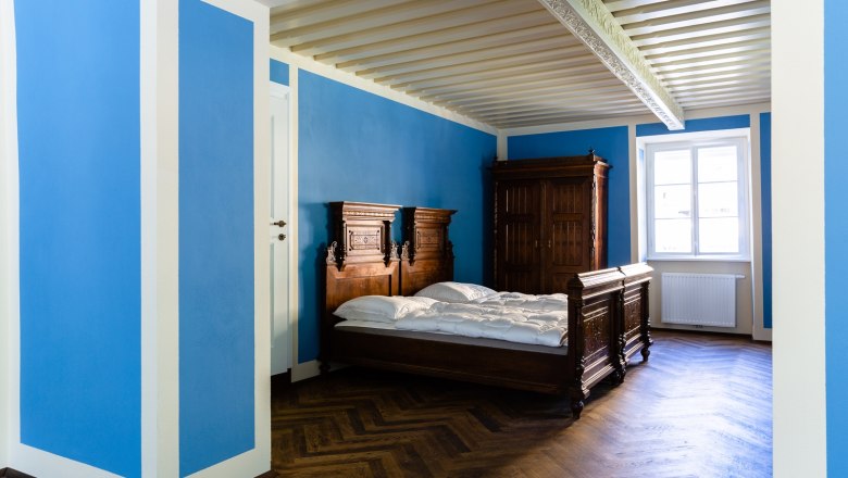 Ein Zimmer mit blauen W&auml;nden, einem Holzbett und einem Schrank.
