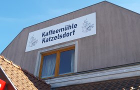 Gebäude mit Schild 'Kaffeemühle Katzelsdorf' und Zeichnung einer Kaffeemühle.