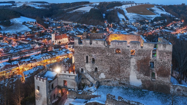 Burgruine Kirchschlag bei Dämmerung mit beleuchteter Stadt im Hintergrund.