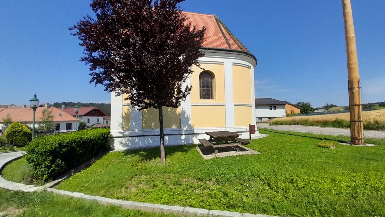Runde Kirche mit gelber Fassade, umgeben von gr&uuml;ner Wiese und B&auml;umen, bei sonnigem Wetter.