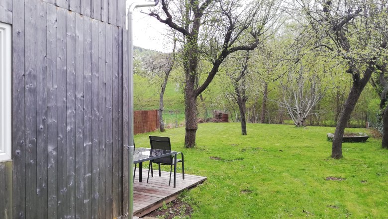 Holzscheune neben Obstgarten mit Tisch und Stühlen auf Holzterrasse.