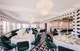 Elegantes Restaurant mit runden Tischen, gr&uuml;nen St&uuml;hlen und Kronleuchtern.