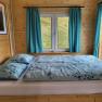 Holzinterieur mit Bett, Fenster und blauen Vorhängen.
