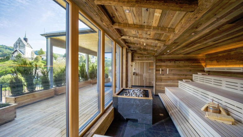 Moderne Sauna mit Holzverkleidung, dunklen Fliesen und Glasfront mit Blick ins Freie.