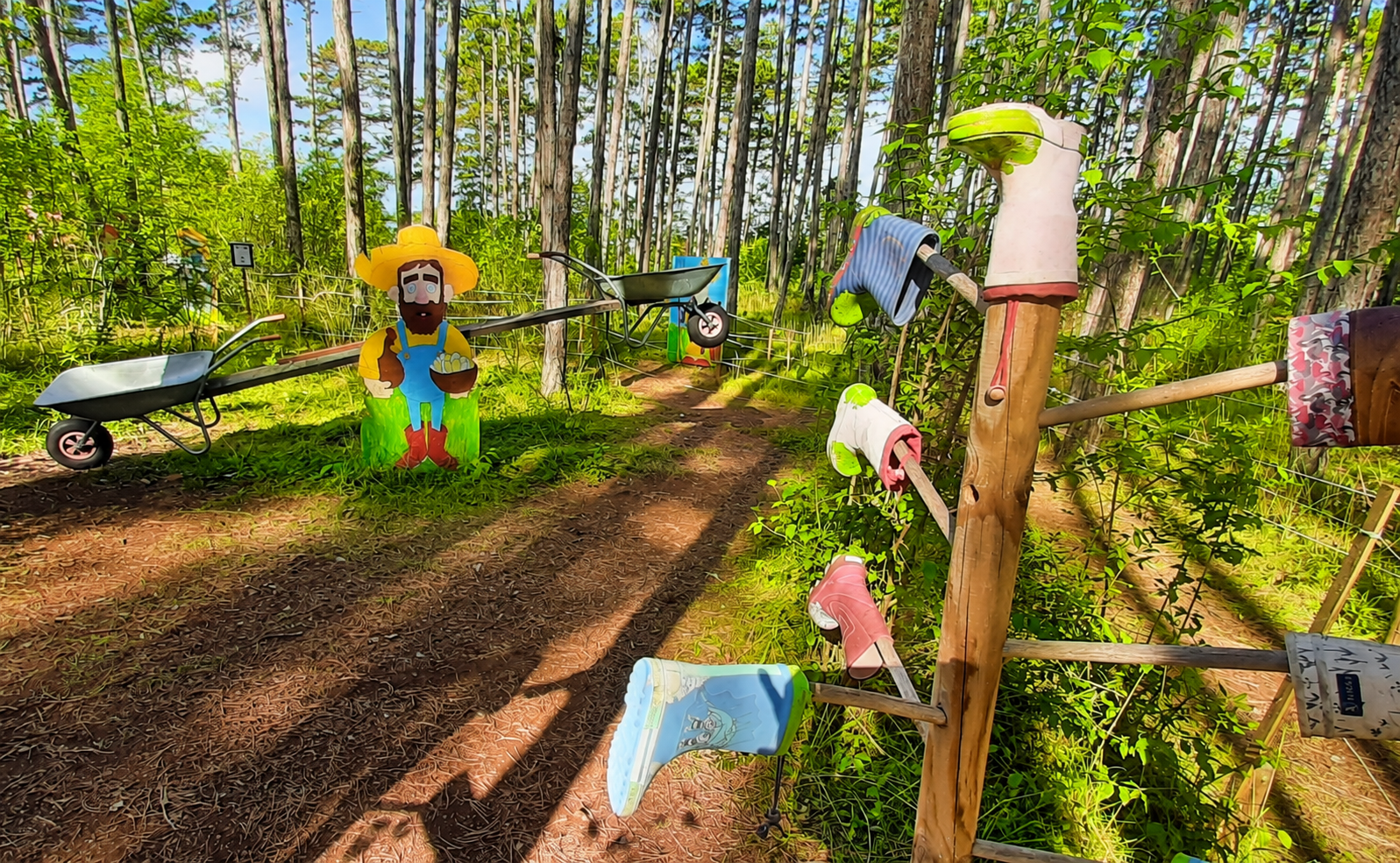 Ein Waldspielplatz mit einer Figur eines Bauern und Gummistiefeln auf Stangen.