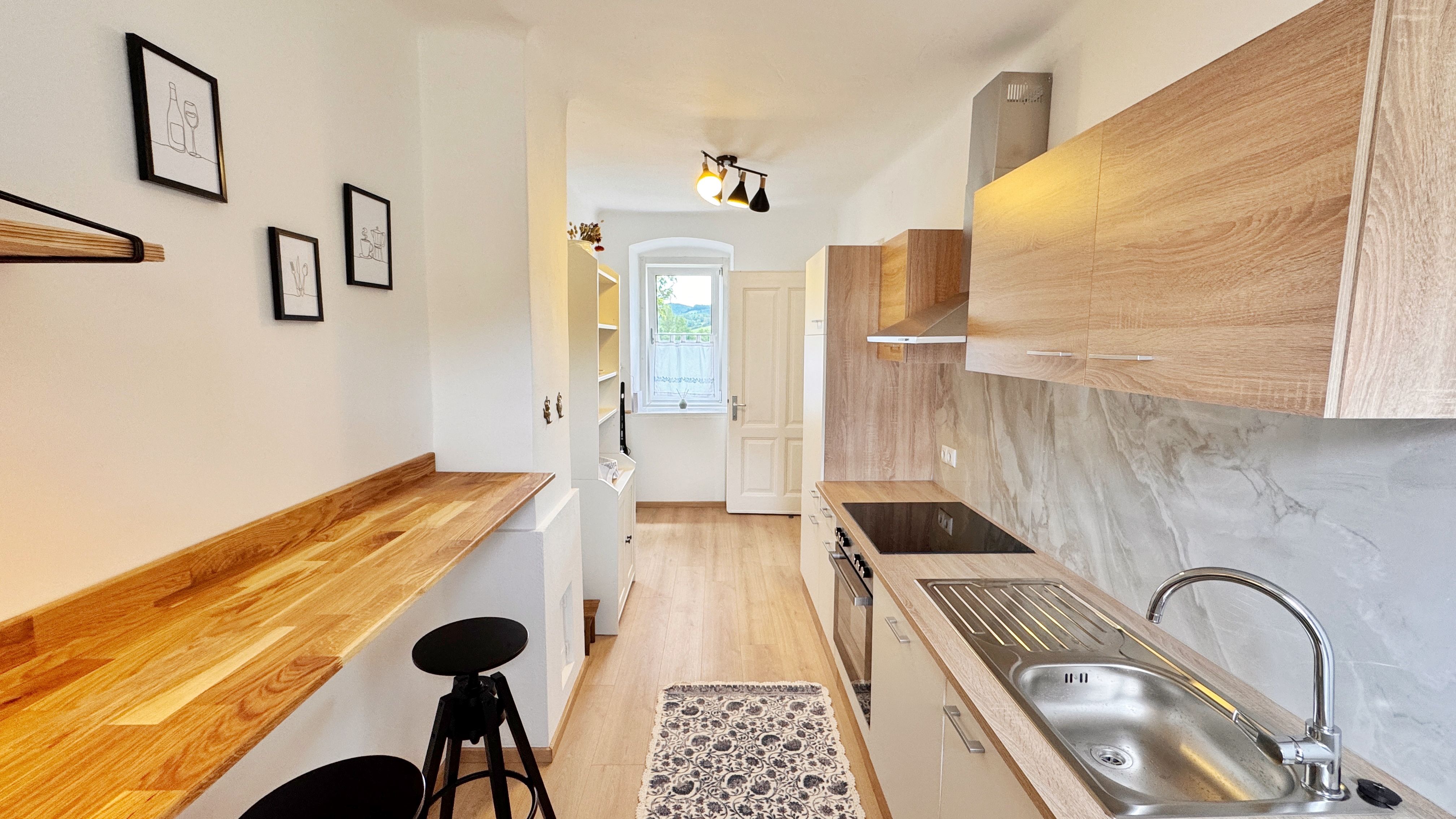 Moderne Küche mit Holzarbeitsplatten, weißen Schränken und Barhockern. An der Wand hängen minimalistische Bilder.