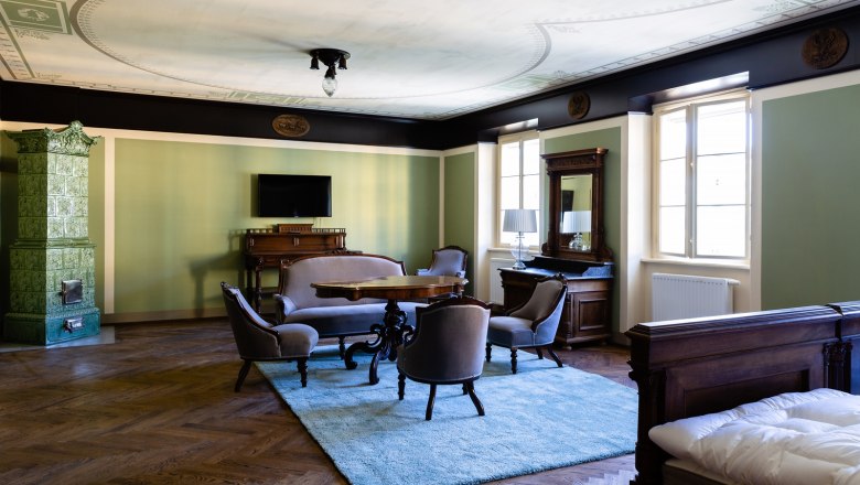 Elegantes Zimmer mit antiken M&ouml;beln, gr&uuml;nem Kachelofen und Teppich.