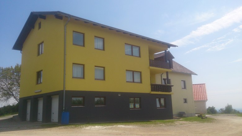 Gelbes Gebäude mit mehreren Fenstern und Balkonen, blauer Himmel im Hintergrund.