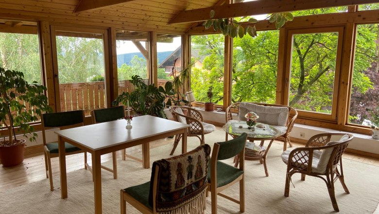 Ein heller Raum mit Holzmöbeln, großen Fenstern und Pflanzen.