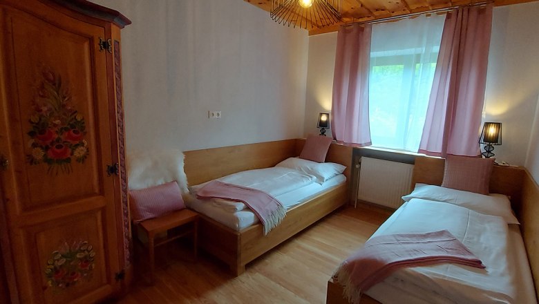 Gemütliches Schlafzimmer mit zwei Einzelbetten, Holzmöbeln und rosa Vorhängen.