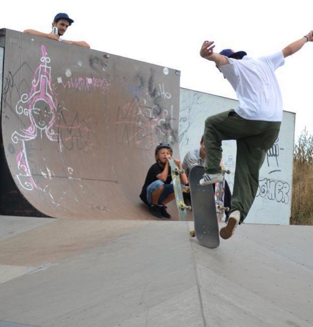 Skateboarder führt Trick auf Halfpipe vor, während zwei Kinder zuschauen.