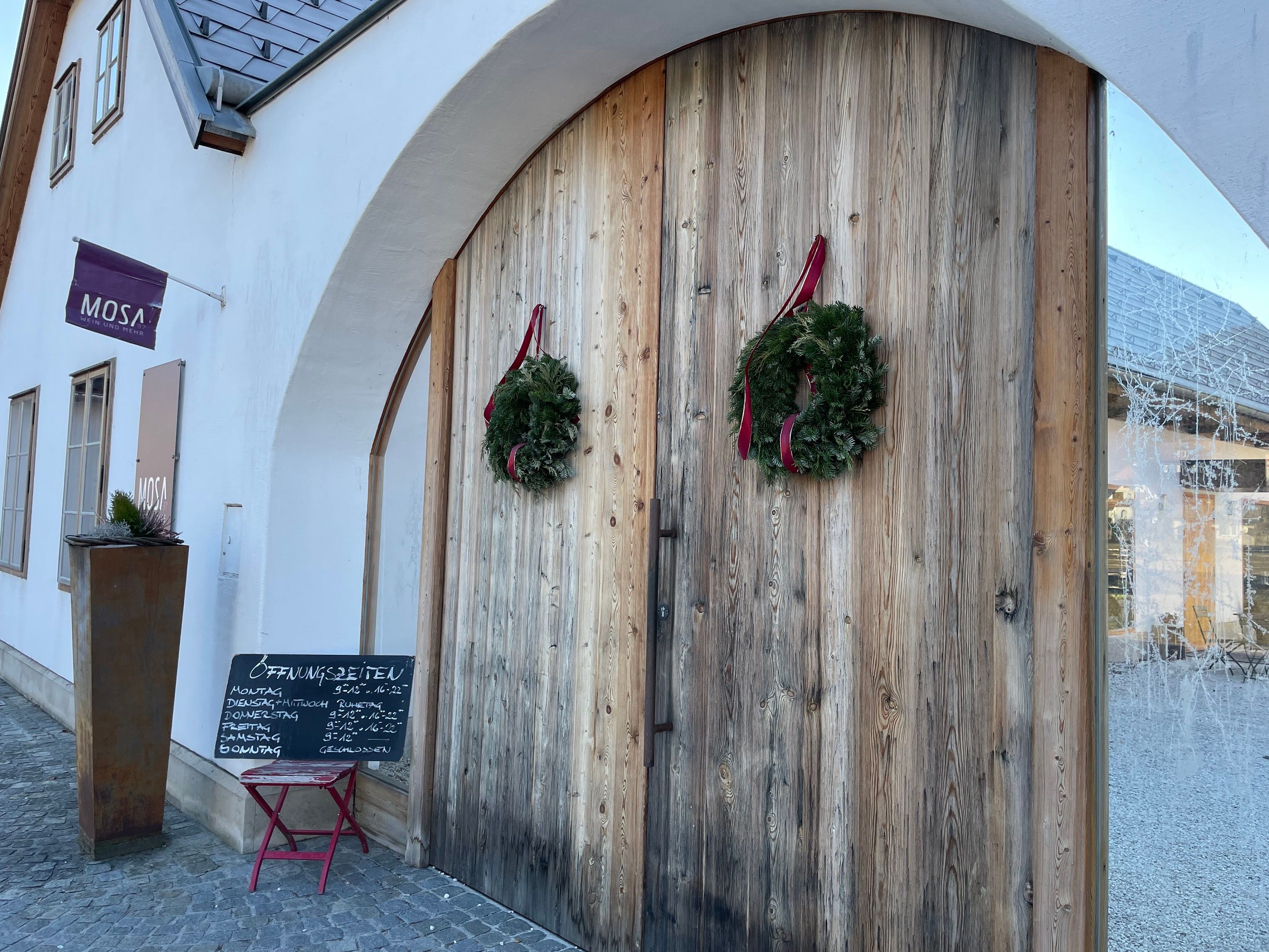 Eingang der Cafe-Bar Mosa mit Holztür und Kränzen.