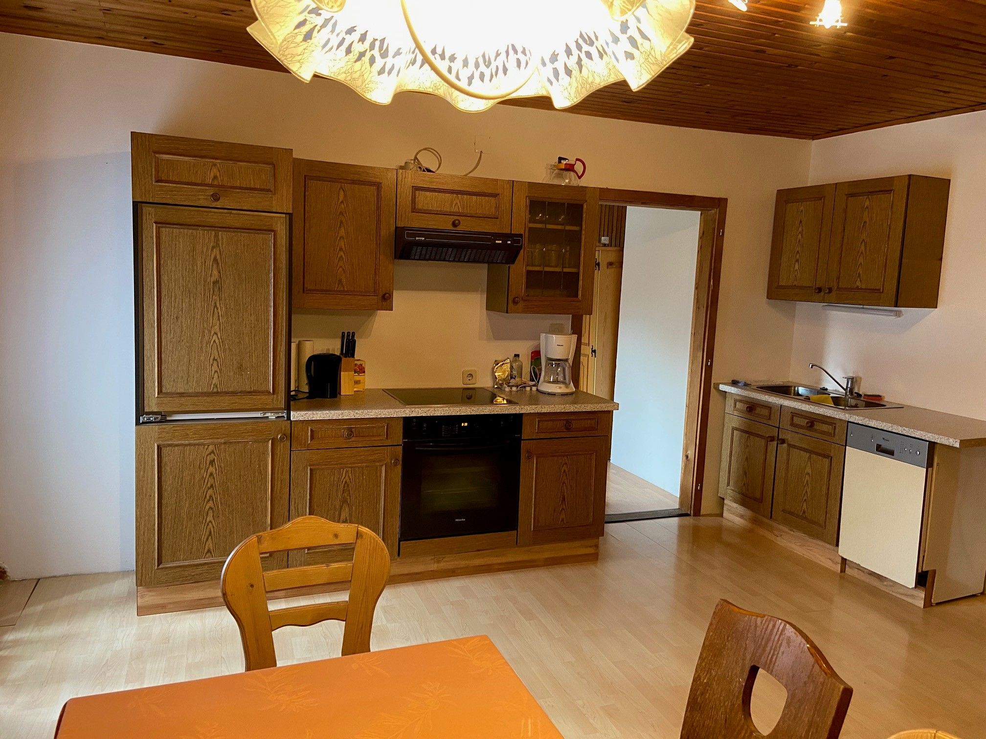 Küche mit Holzmöbeln, Esstisch und Stühlen, Herd, Spüle und Geschirrspüler.