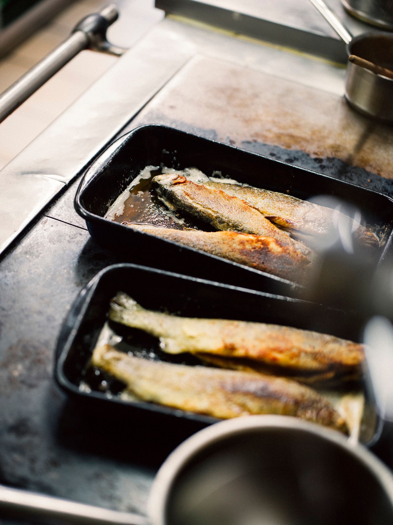 Two fried trout in a black baking dish on a stove.