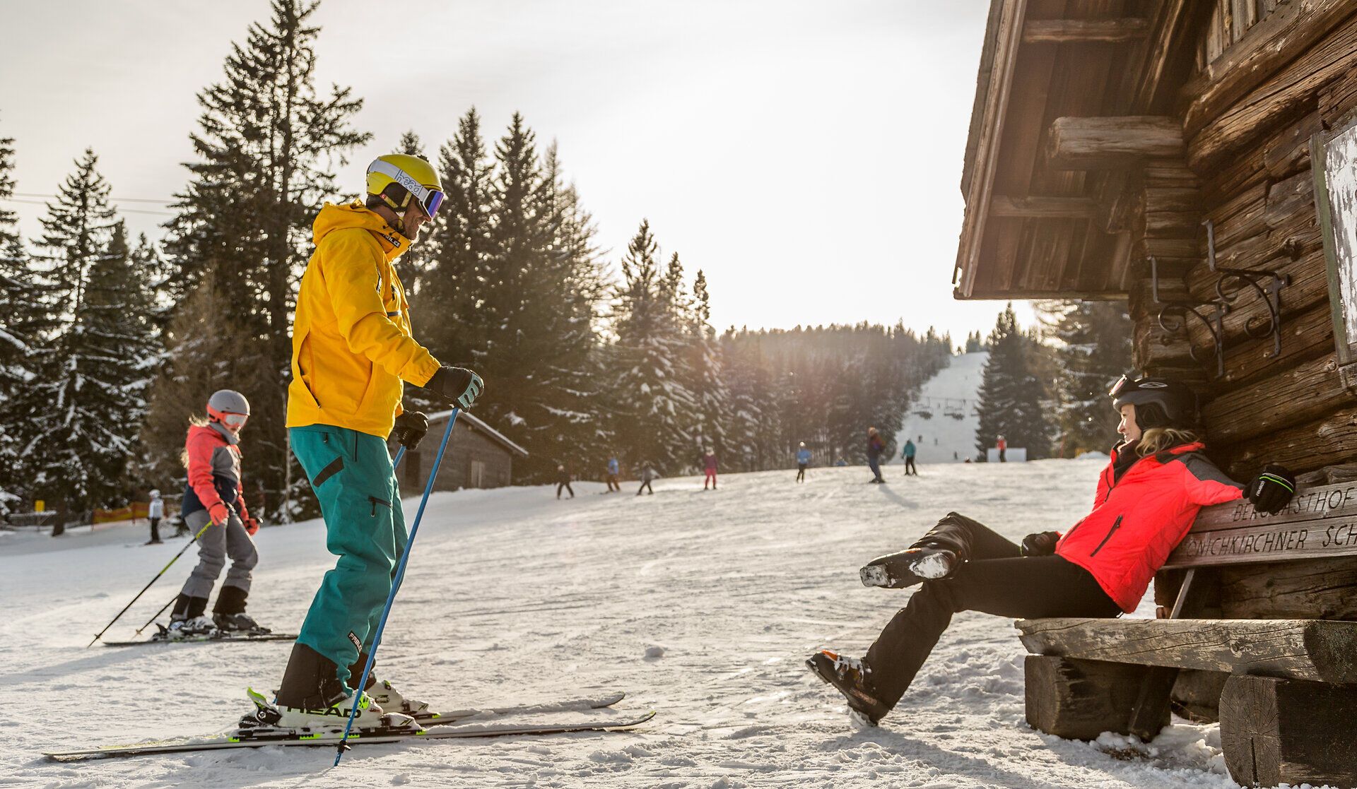 Die verschneite Landschaft lädt zu einem unvergesslichen Winterabenteuer ein. Skifahrer gleiten sanft über die Pisten, während die Sonne hinter den Bäumen strahlt und eine magische Atmosphäre schafft.