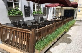 Outdoor area of a restaurant with wooden fence, tables and red parasols.