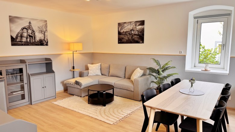 Moderner Wohn-Essbereich mit grauem Sofa, Esstisch und Pflanzen.