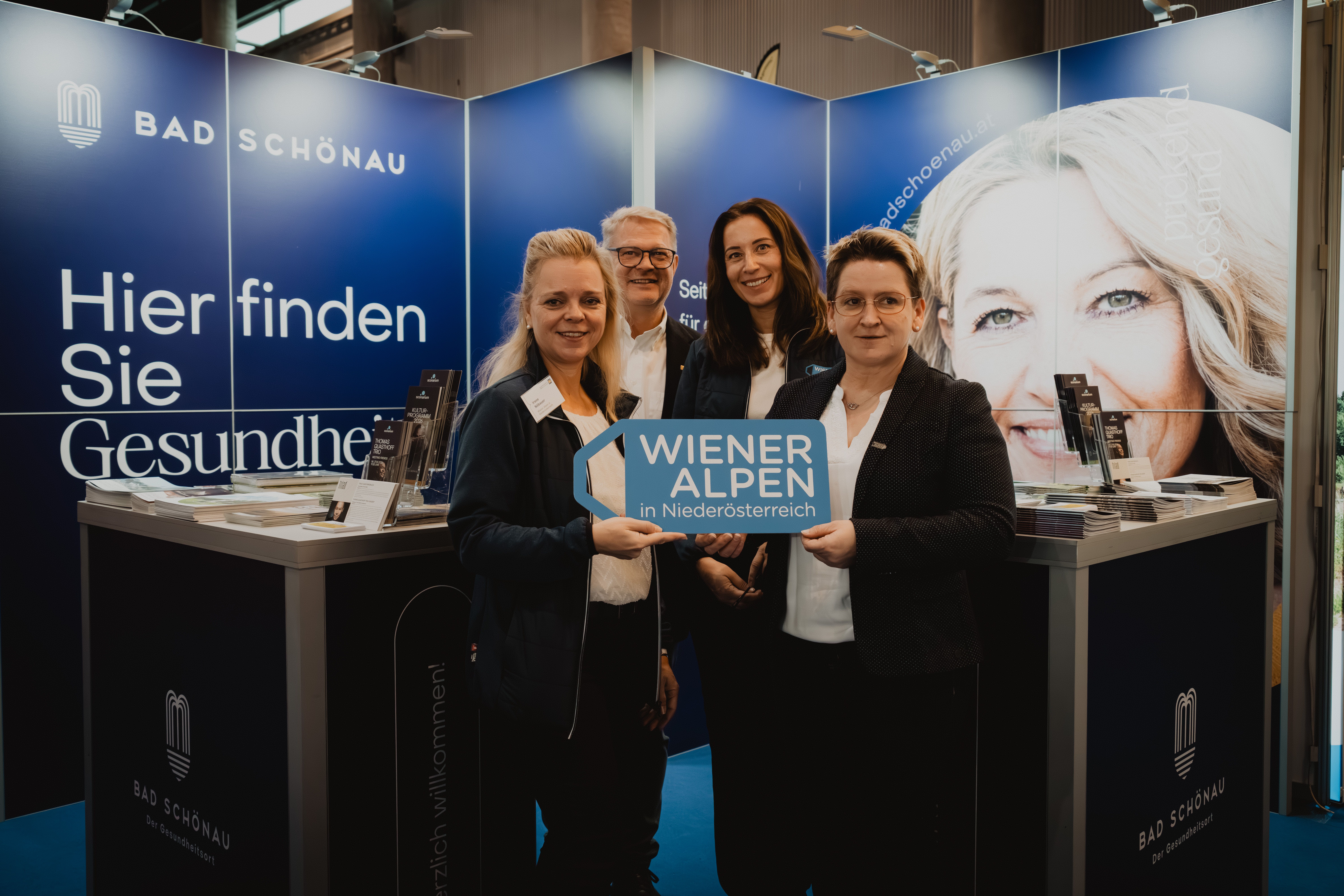Drei Damen und ein Herr mit dem Schild Wiener Alpen in Niederösterreich vor dem Messestand Bad Schönau 