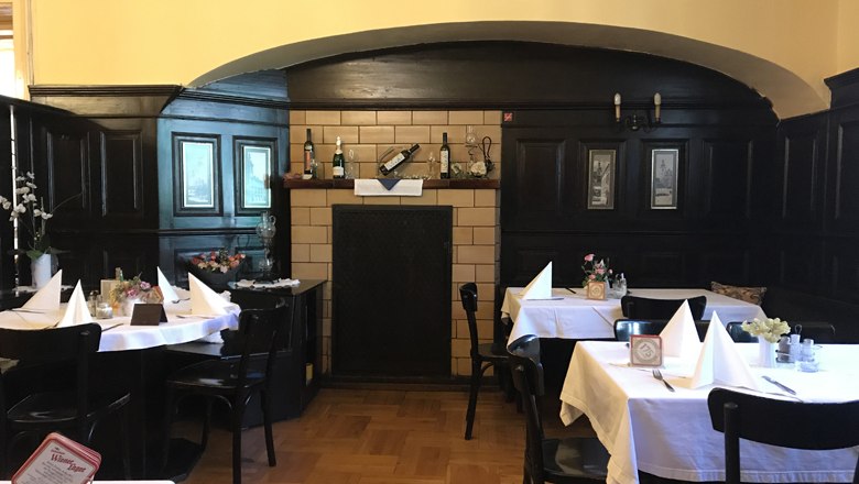 Innenansicht eines traditionellen Restaurants mit dunkler Holzvertäfelung und gedeckten Tischen.