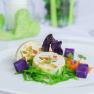 Artfully arranged corn roulade, purple potato cubes and green garnish on a white plate.