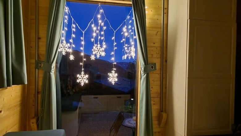 Window with curtains and snowflake fairy lights, two candles on the windowsill.