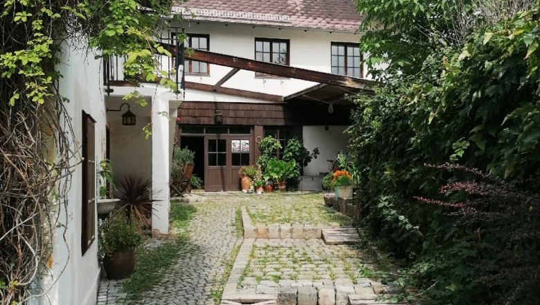 Gepflasterter Hofeingang mit Pflanzen und einem wei&szlig;en Geb&auml;ude im Hintergrund.