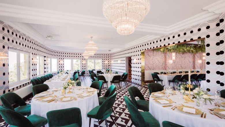 Elegantes Restaurant mit runden Tischen, grünen Stühlen und Kronleuchtern.