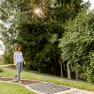 A woman walks barefoot on a green path in the spa gardens of Bad Sch&ouml;nau, surrounded by trees and sunlight.