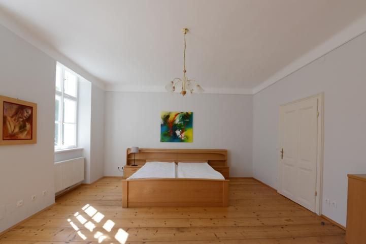 Schlafzimmer mit Holzboden, Doppelbett, zwei Gemälden und einem Fenster.