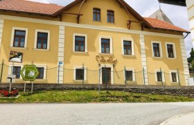 Gelbes Gebäude mit der Aufschrift 'Villa Luef', umgeben von einem Zaun und einer Straße im Vordergrund.