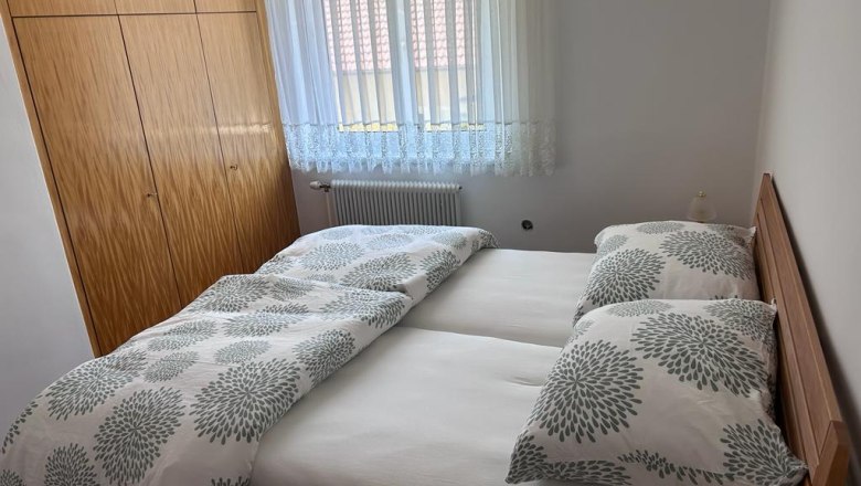 Ein Schlafzimmer mit einem Doppelbett, wei&szlig;en Vorh&auml;ngen und einem Holzkleiderschrank.
