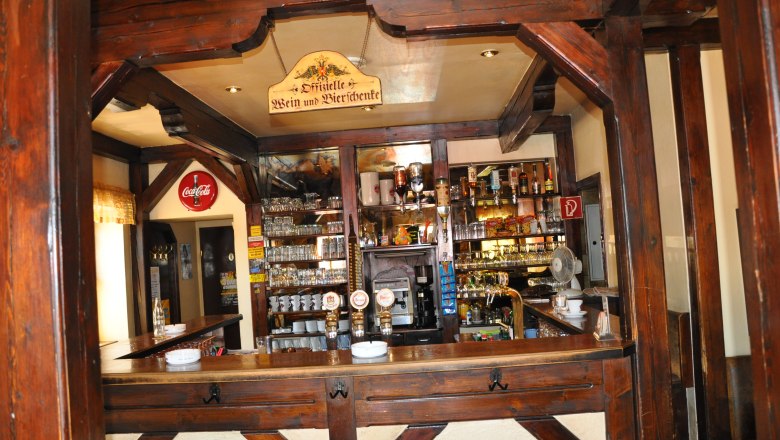 Innenansicht einer rustikalen Bar mit Holzbalken und einer gut bestückten Theke.