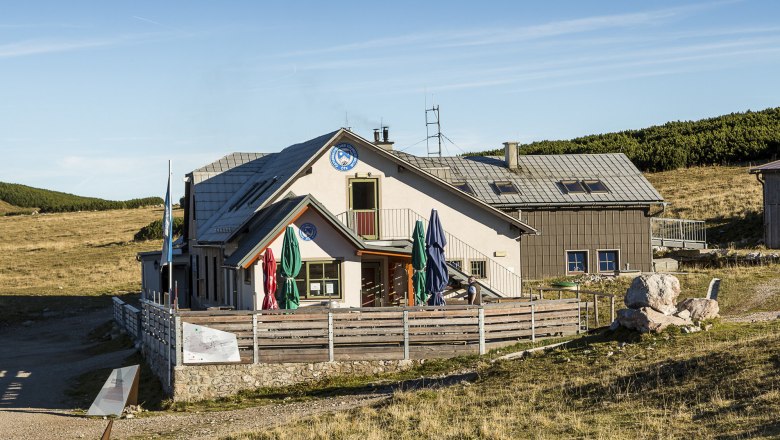 Das Damböckhaus am Schneeberg in einer sonnigen Berglandschaft mit blauem Himmel.