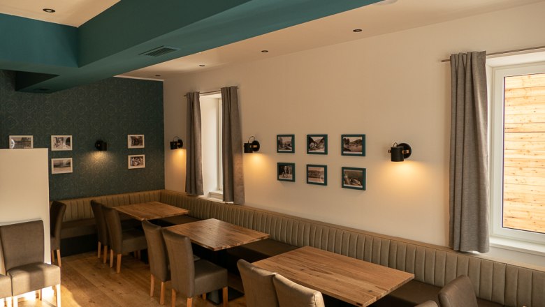 Innenansicht eines Restaurants mit Holztischen, gepolsterten Bänken und Stühlen, dekoriert mit Bildern an den Wänden.