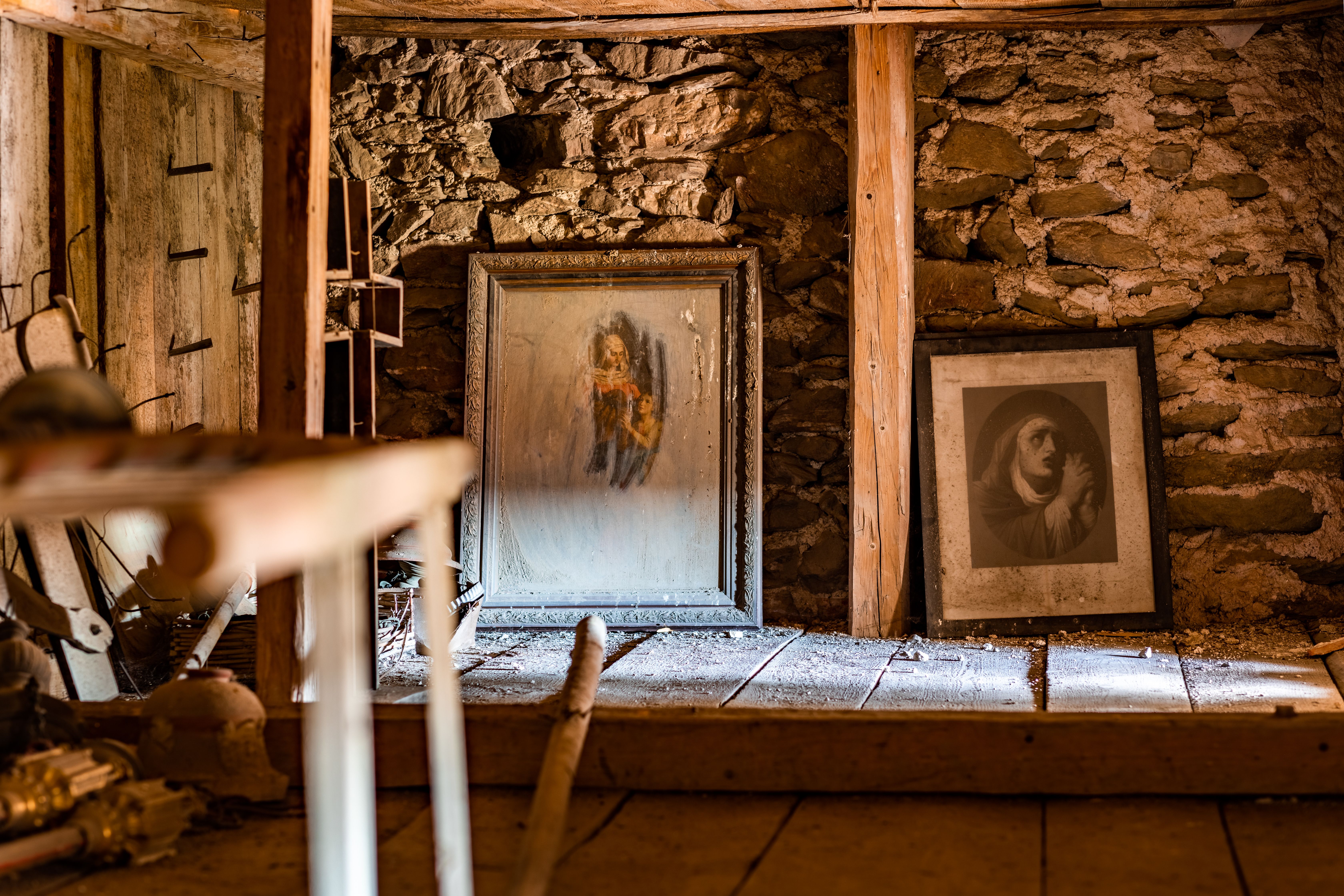 Verstaubte Bilder mit christlichen Motiven vor einer Steinmauer am Dachgeschoss der Wehrkirche Lichtenegg