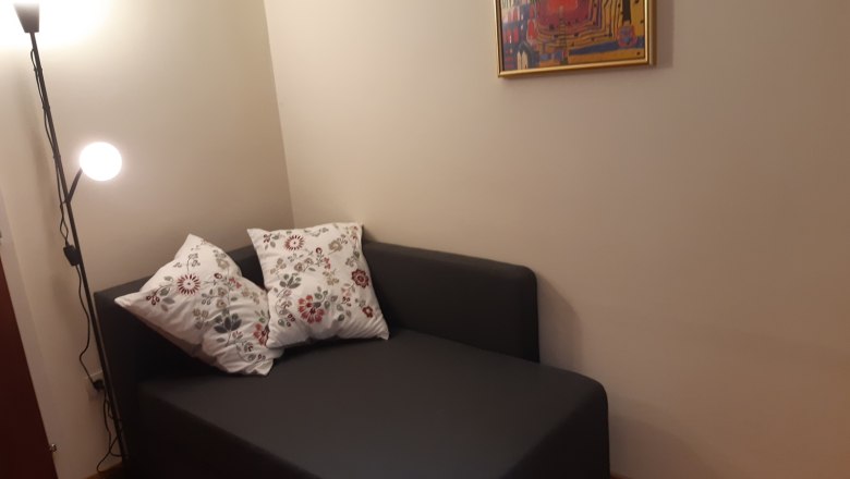 Gem&uuml;tliche Leseecke mit grauem Sofa, zwei gemusterten Kissen, Stehlampe und abstraktem Bild an der Wand.
