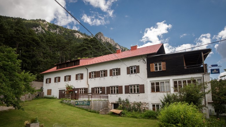 A large building with a red roof in front of a wooded hillside.