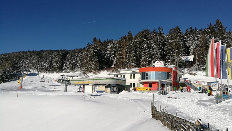 Sesselliftstation in Mönichkirchen im Winter mit schneebedecktem Gelände und Wald im Hintergrund.